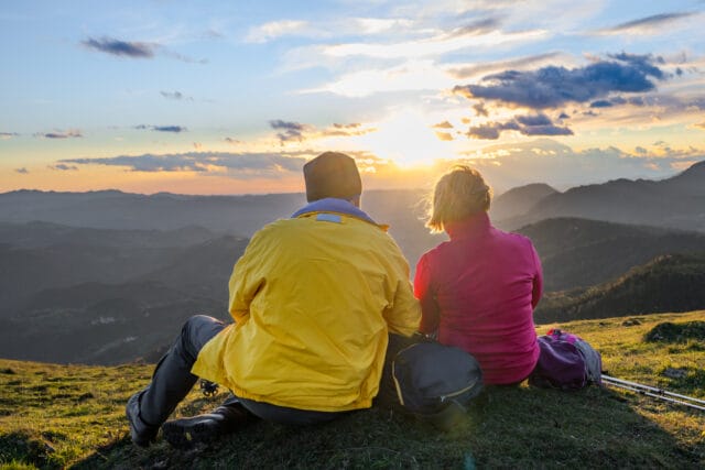 Parents relaxing in mountains, admiring sunset.